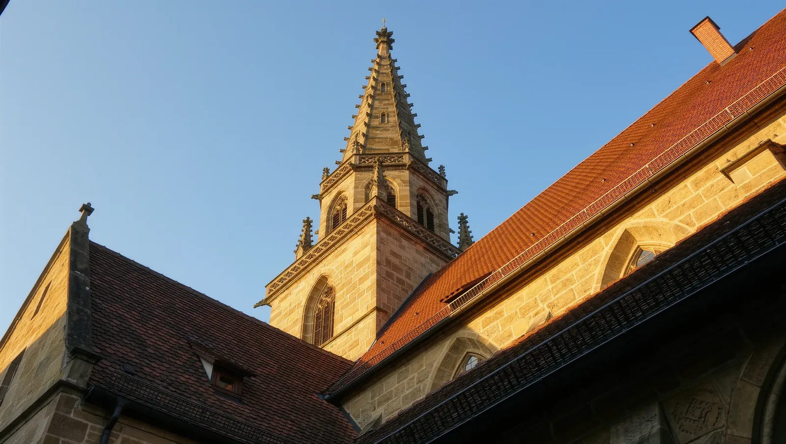 Symbolbild Kirchturm über Ziegeldächern